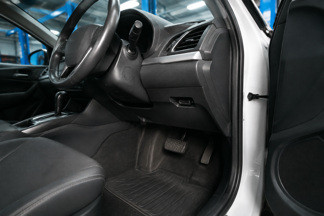 Unbranded car driver footwell in a blue-lit workshop with a visible OBD2 diagnostic port beneath the dashboard.